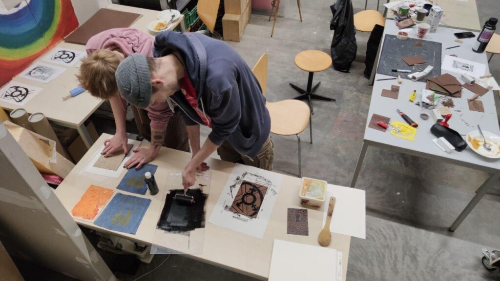 Zwei Menschen stehen an einem Tisch in der Offenen Werkstatt und arbeiten mit dem Linoldruck verfahren